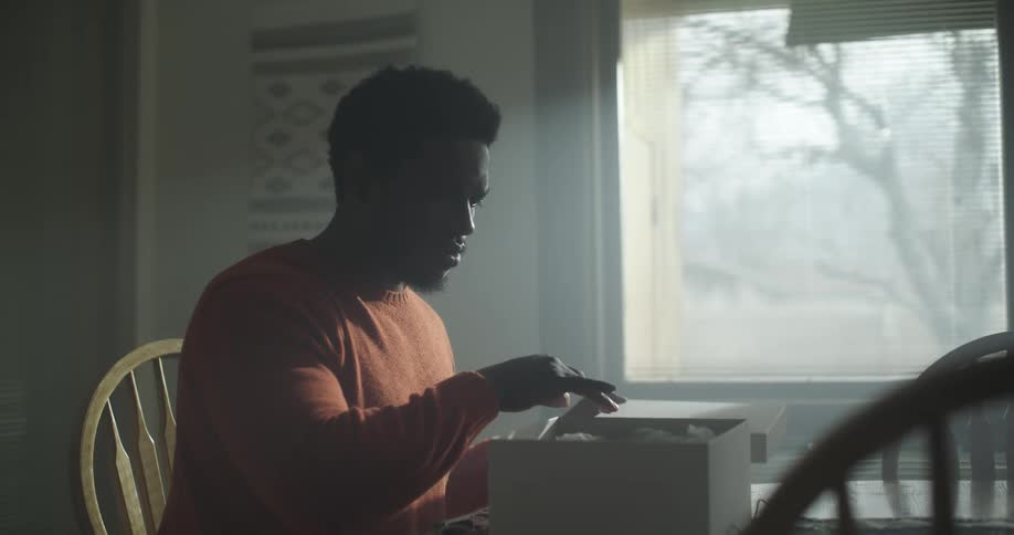 A man sits at a table opens a box and pulls out an item