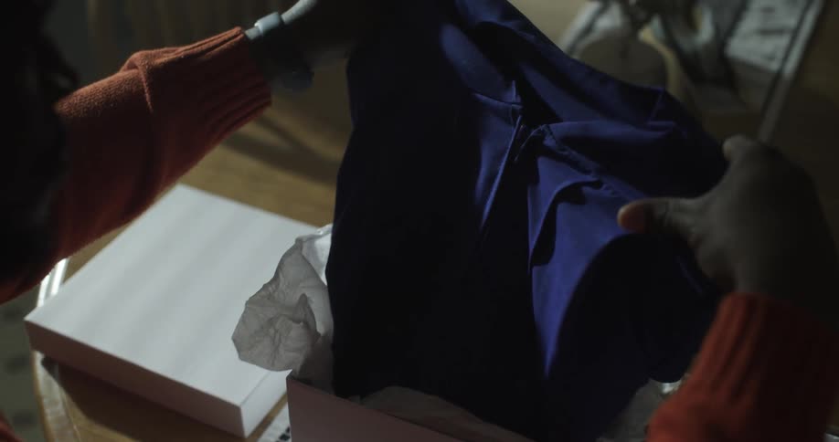 Man opens a box and removes a garment from it and holds it up