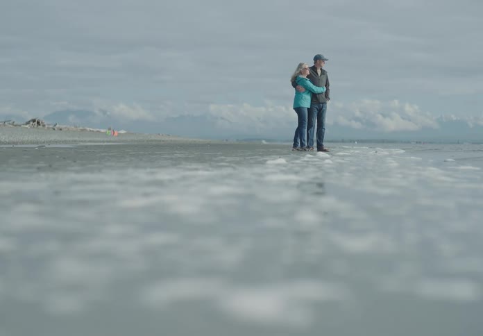 A man and a woman standing on a shore hugging with the sky in the background