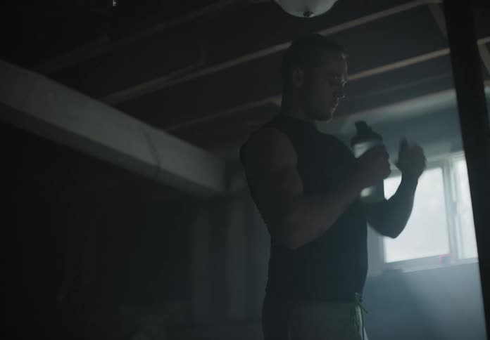 A white man drinks water while standing in a basement