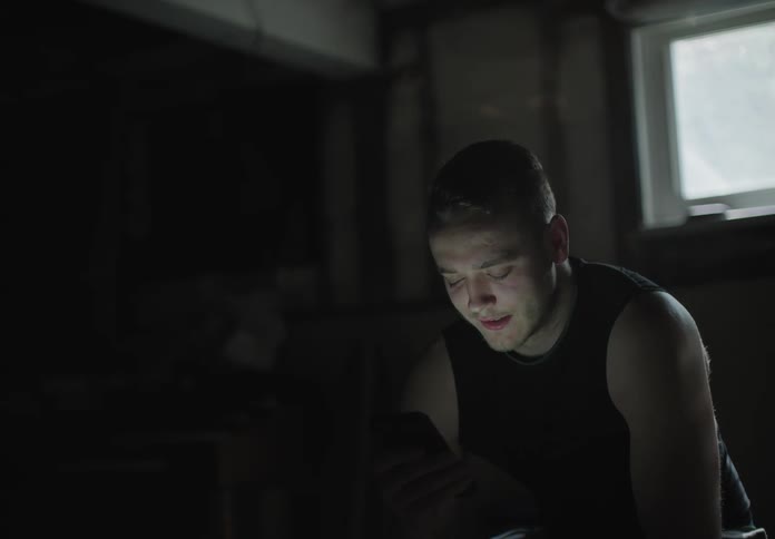 A man sitting in a basement video chatting on a smart phone