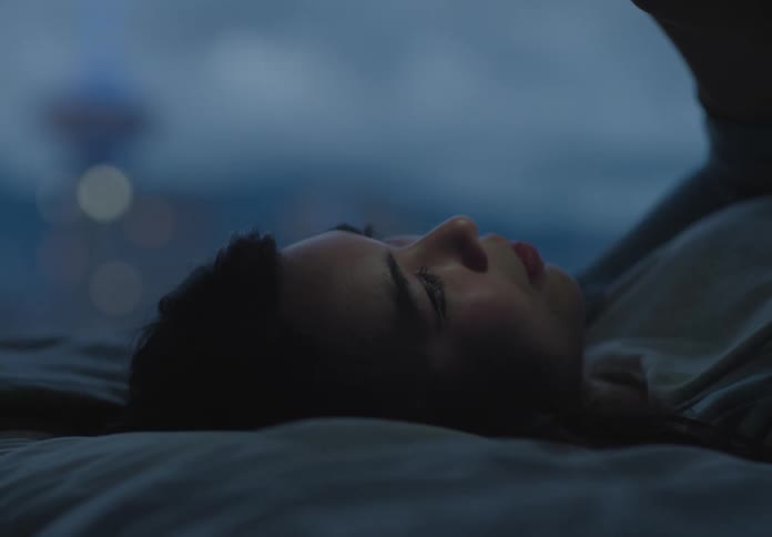 An asian woman lies in bed scrolling through a smartphone