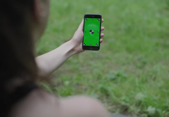 A woman looking at a smart phone with grass in the foreground