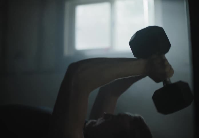 Man working out lifts dumbbells in a dimly lit basement
