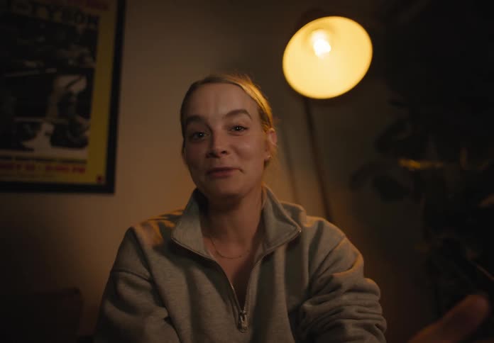 A white woman sits in a room and smiles and talks