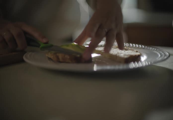A white woman spreads guacamole on pieces of bread on a plate