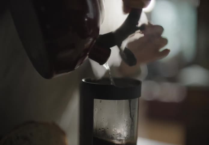 A person pouring hot water from a kettle into a glass