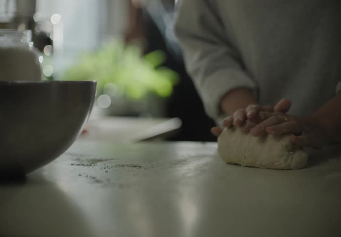 Female kneading a ball of dough on a kitchen counter that is dusted with flower