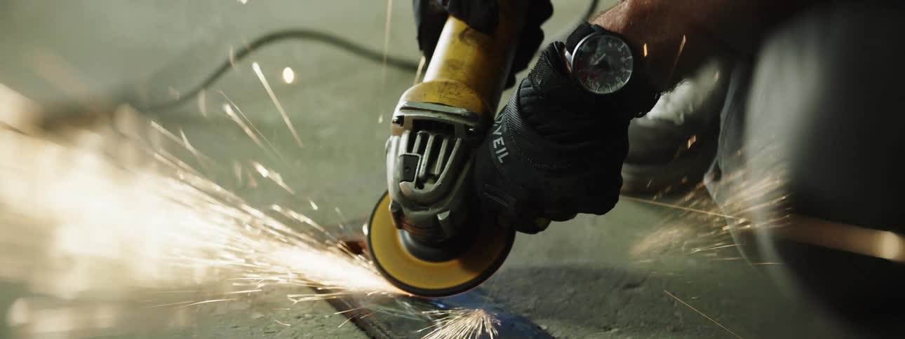 A worker uses a handheld saw to cut into a piece of metal