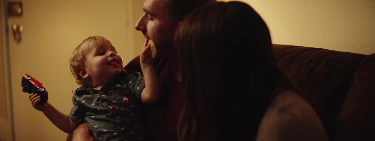 A dad holds his son on his lap with his wife beside him as they both tickle and play with their child