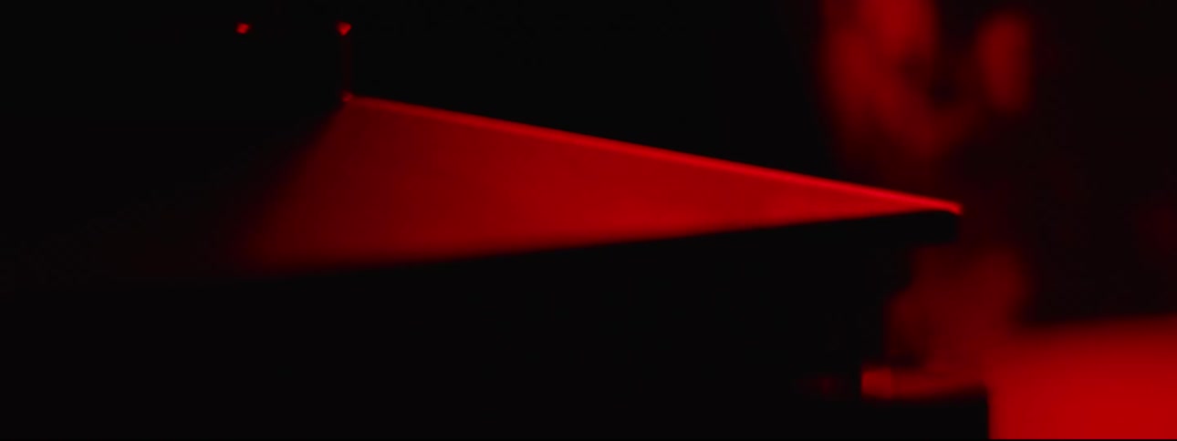 A red light glows and reflects on a piece of angled metal as it lowers into a box