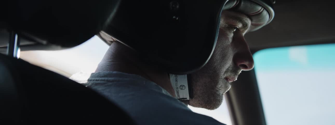 A man wearing a helmet sits in a car and takes a deep breath