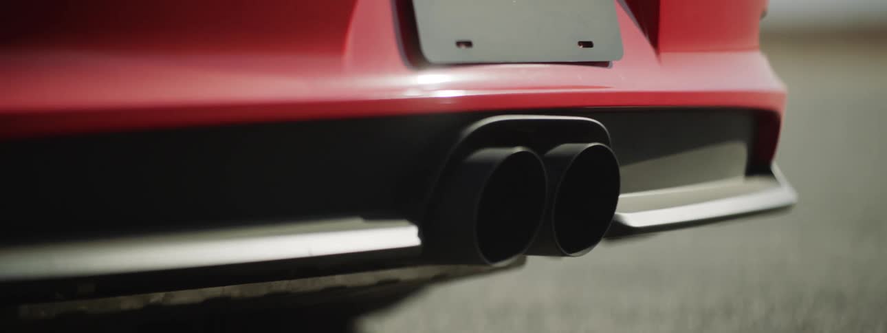 Red vehicle with twin exhaust ports parks on asphalt