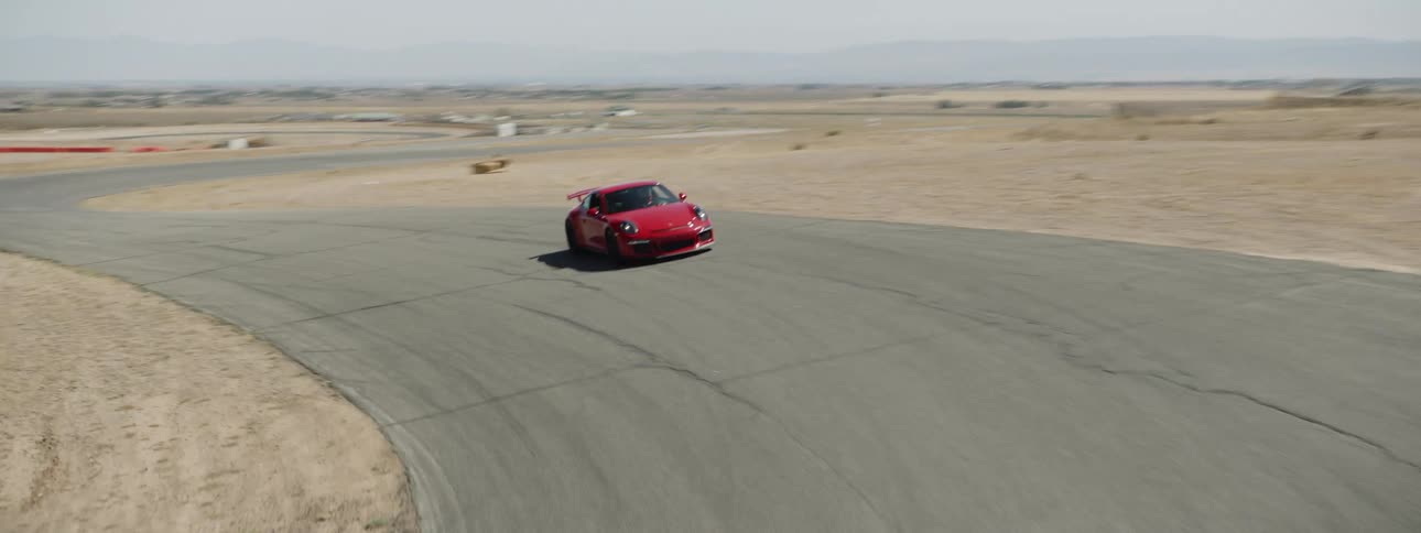 A red racing car drives down a track in the middle of a desert