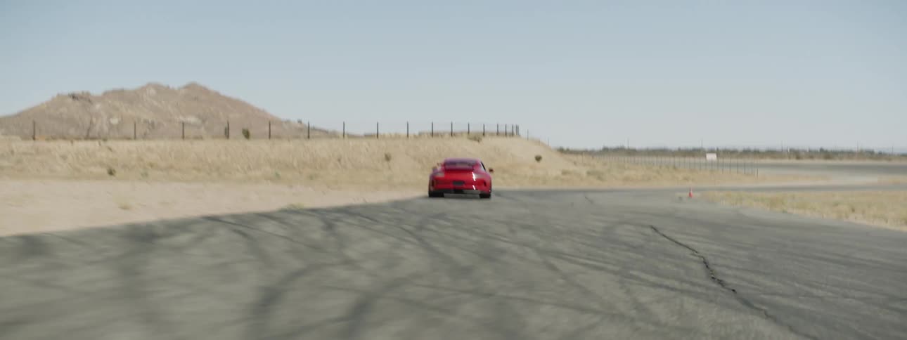 Red sports car races down winding road between fields with low mountains on the horizon