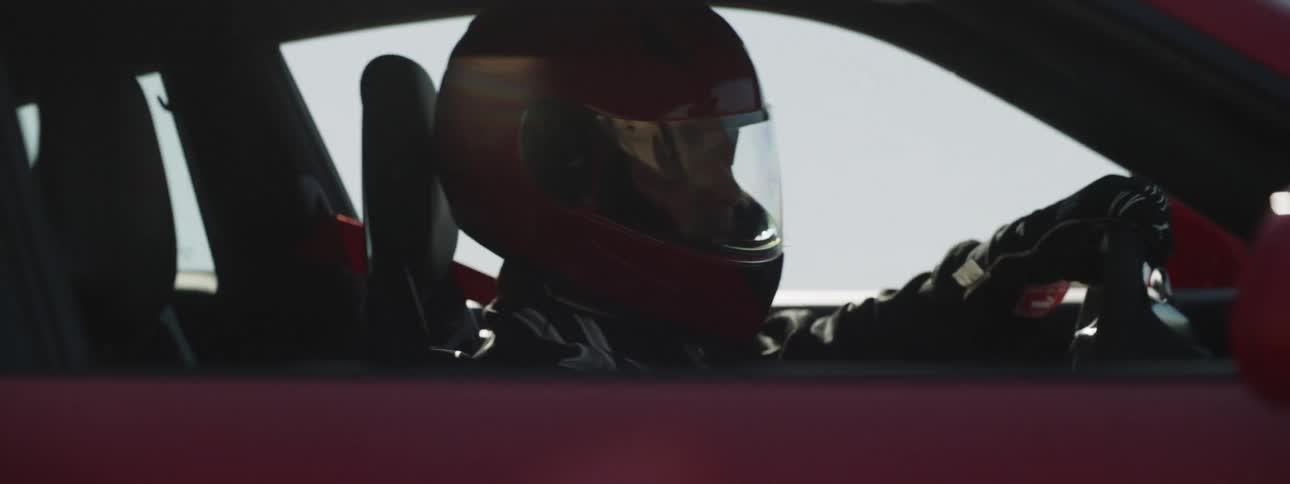 A driver wearing a helmet and gloves races on a desert road in red sports car