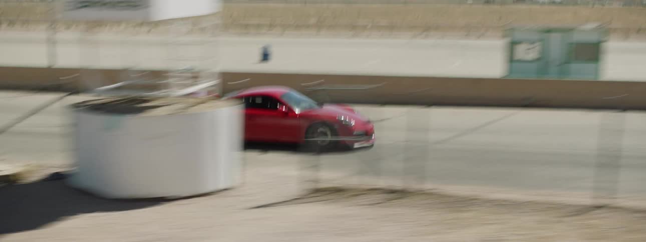 Red sports car races along road past mowed fields