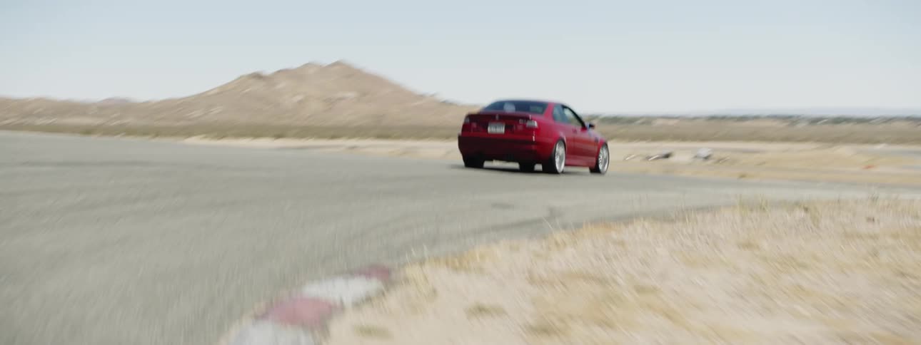 A red car races down a track in the desert