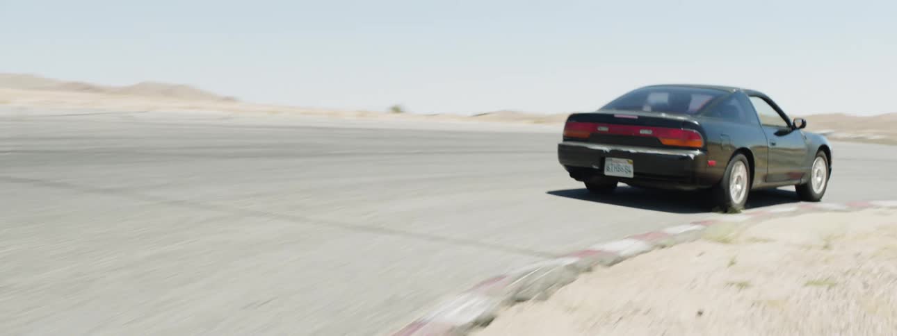 A sports car drives around a turn in a race track out in a desert