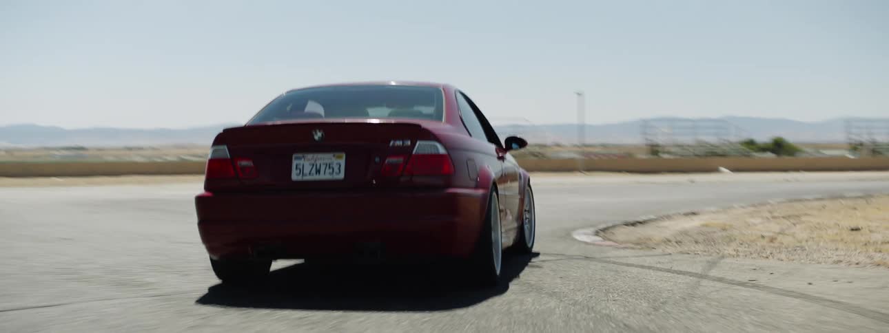 A red bmw speeds around a turn in an empty desert track