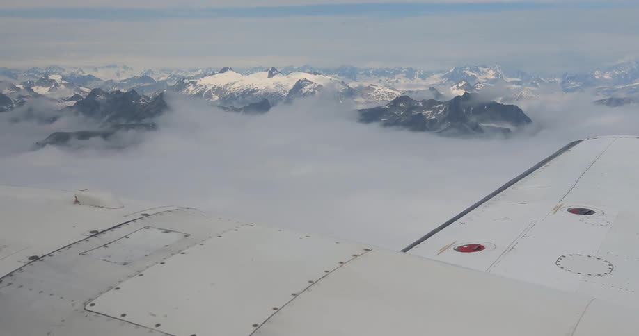 Aerial view from a plane window of a wing and the clouds over a mountain