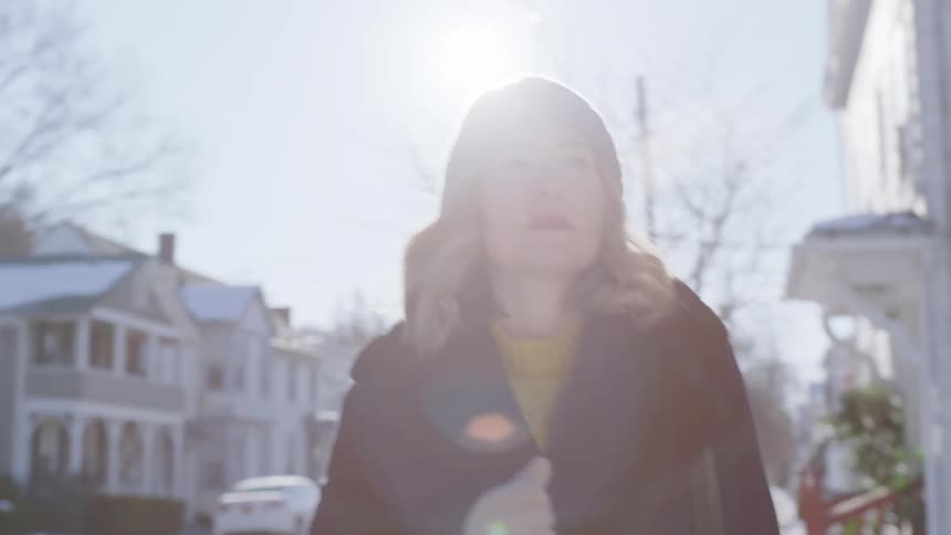 A woman walks down a sidewalk carrying a basket on her arm on a bright sunny winter day