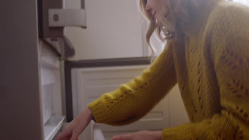 A woman opens the bottom freezer and places food items in the drawer