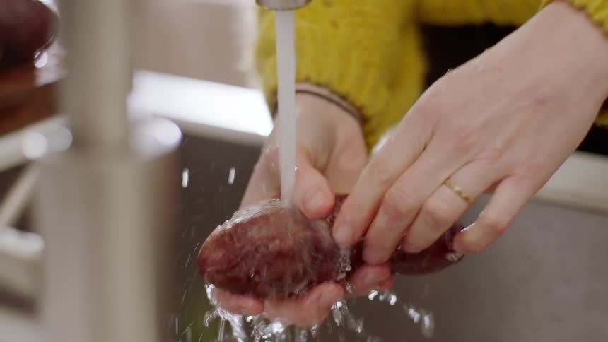 Female washing a potato under the faucet in the kitchen sinking as she rubs it with her fingers to remove all of the dirt