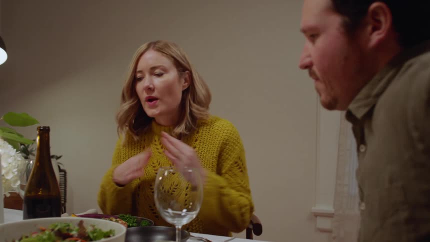 A couple sits down at a dining table to have a meal and a glass of wine