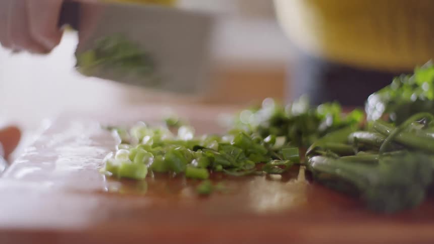 A white woman cuts and dices a pile of greens in a kitchen