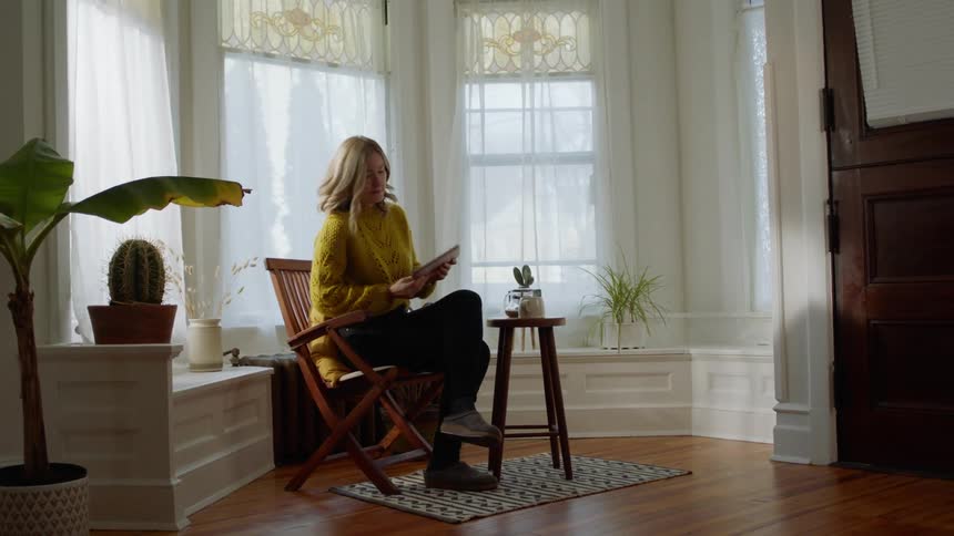 Woman reaches for a laptop as she sits on a wooden chair