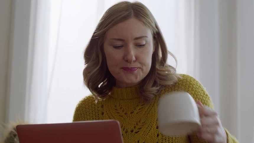 A woman sitting down looking at a laptop sipping on coffee