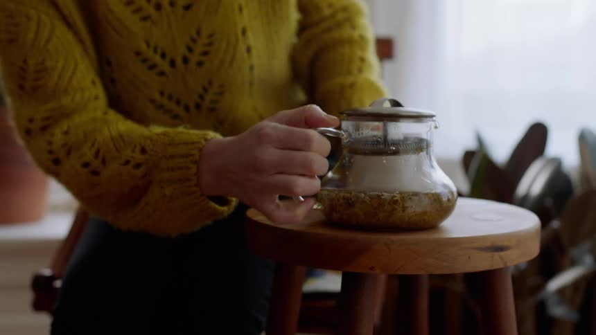 Woman sits down in chair and pours tea into mug