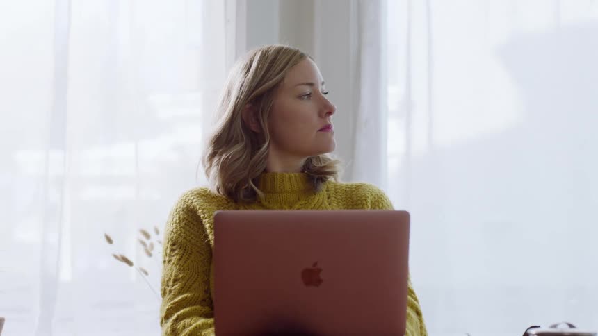 A woman in a yellow sweater types on a mac laptop at home