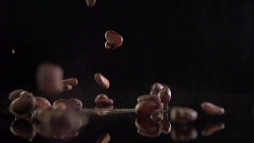 Coffee beans fall on a dark reflective surface