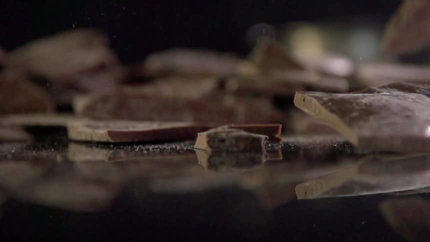 Chocolate falls and shatters on a reflective surface