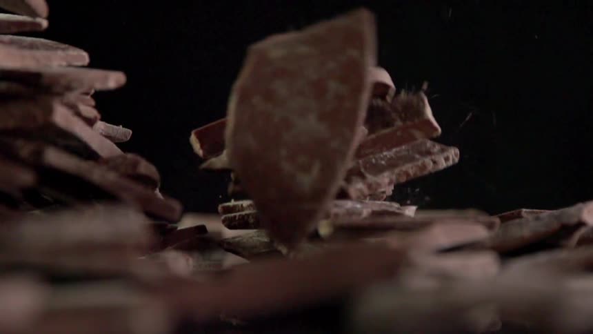 Broken pieces of chocolate bar fall in a pile against a black background