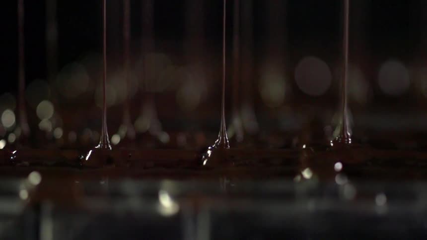 Melted chocolate drips from a machine onto a stainless steel surface