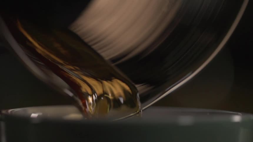 Coffee pours out of a small pitcher and into a cup