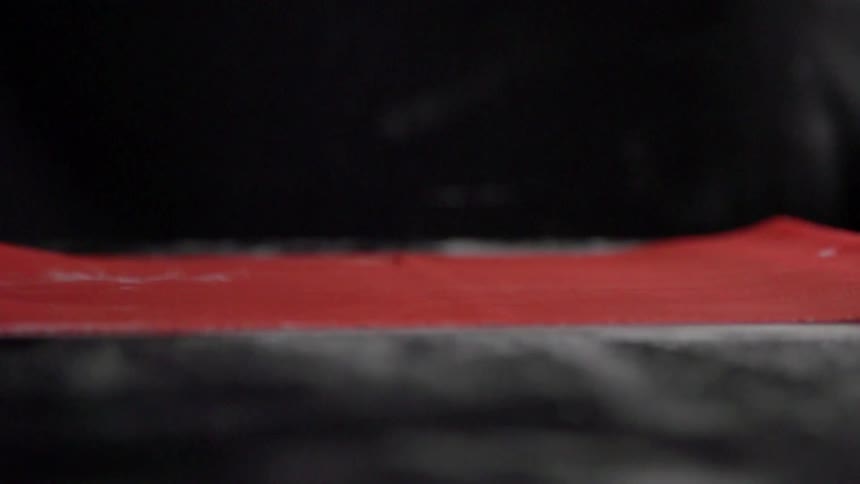 A black gloved hand slides a think piece of red food material across a black table