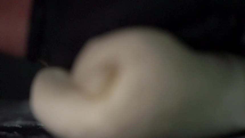 Person wearing black latex gloves rolls and kneads dough