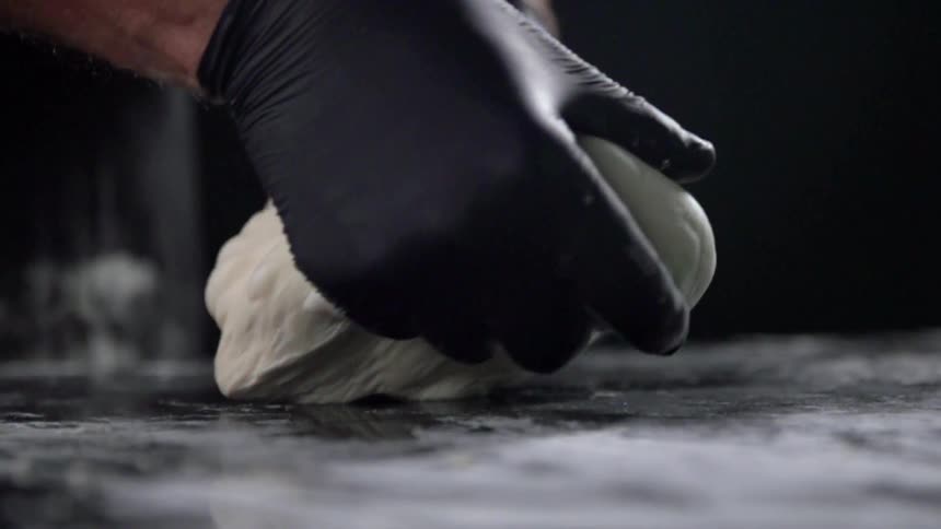 Person wearing black gloves kneads dough on marble surface
