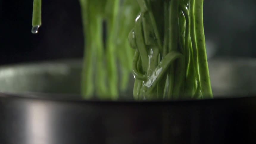 Green pasta noodles being lifted from water in pot