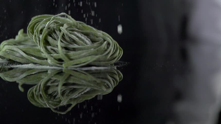 Parmesan cheese falls onto a pile of pasta noodles