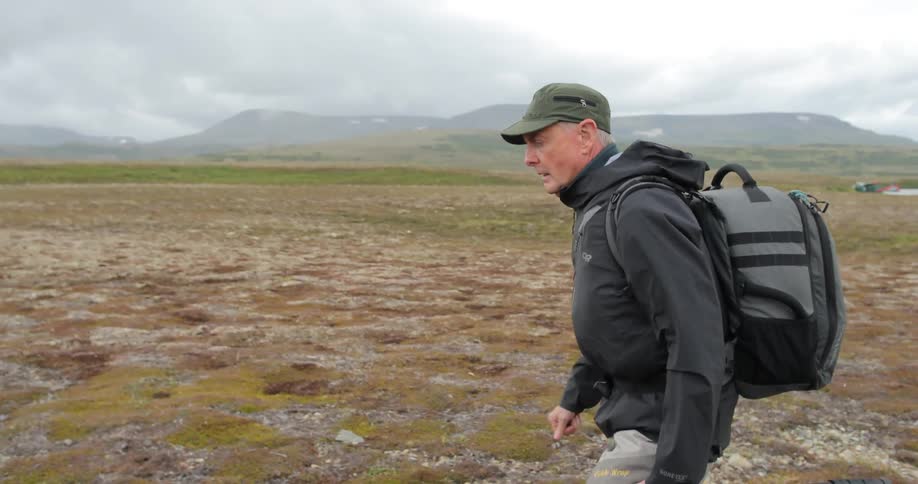 A man carrying a tripod hikes across a plain