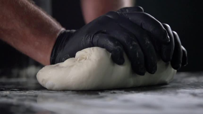 Gloved hands kneading dough