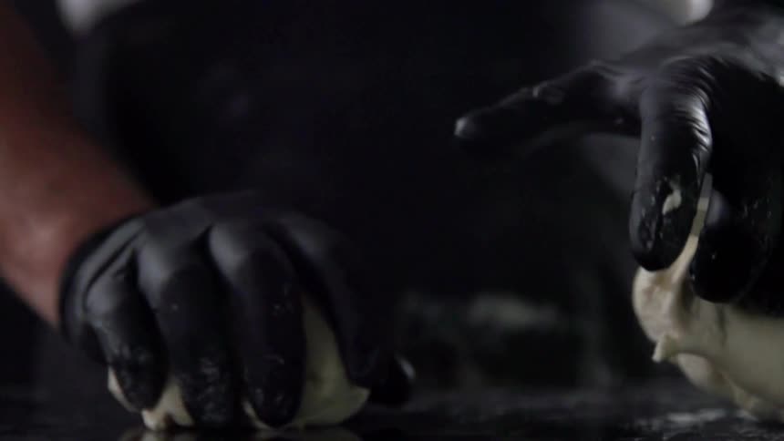 A person with black gloves and an apron kneading dough