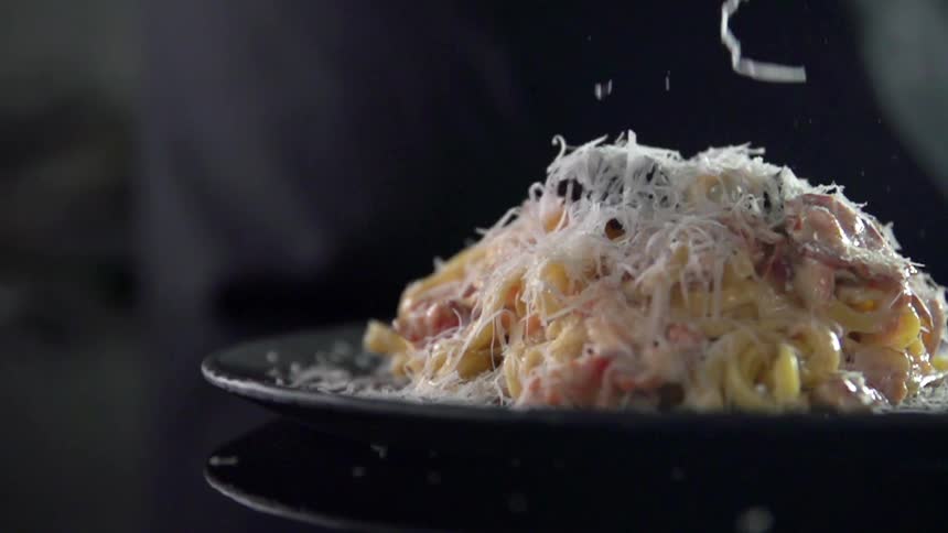 Grated cheese is added to a plated entree on a black table