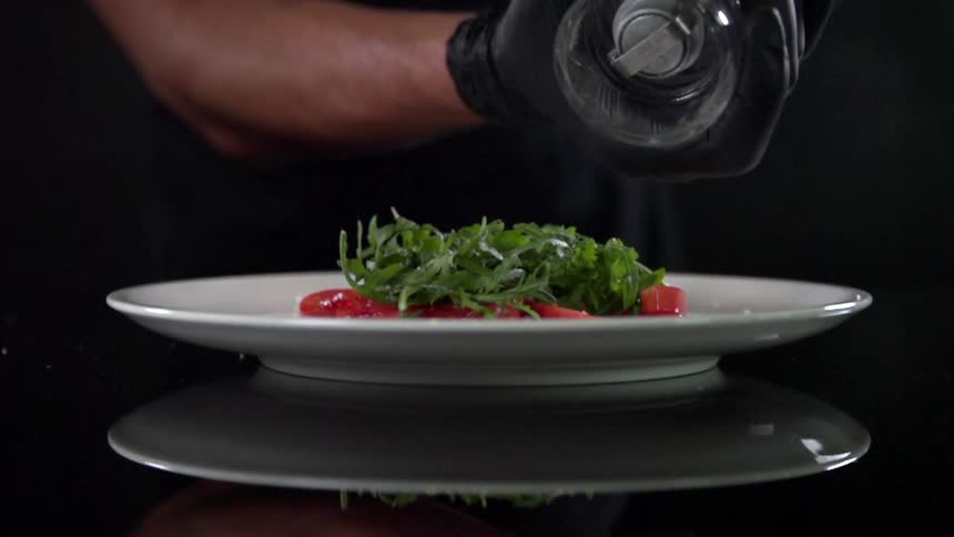 A man spreading seasoning on a vegetable dish in a dark studio