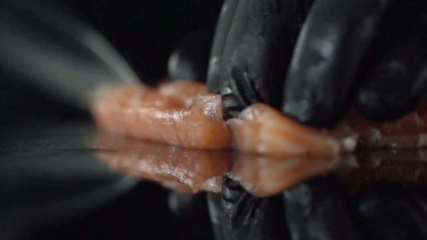 A person wearing a black glove cuts a piece of meat with a knife